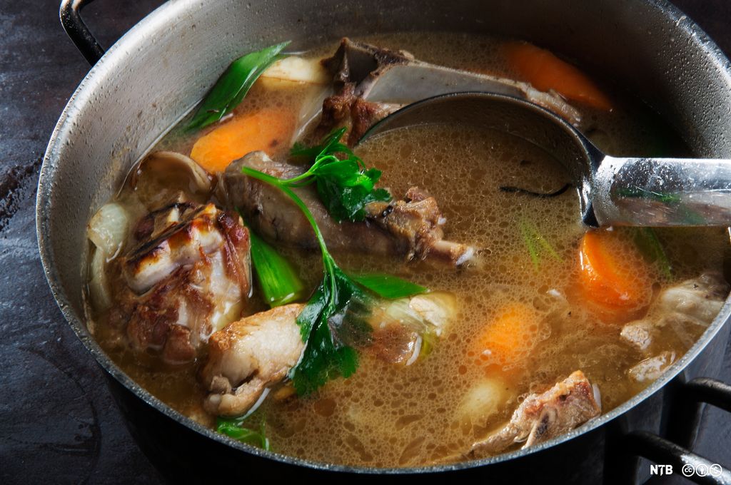 Kraft av lammebein, gulrot, purre, sellerirot og persille står til koking i en kjele. Foto.