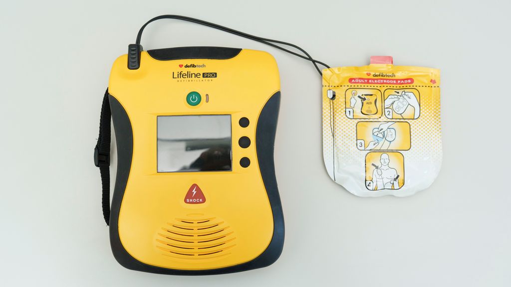 Hjertestarter med fem knapper og et display. Et elektrodesett er koplet til hjertestarteren med en ledning. Foto.