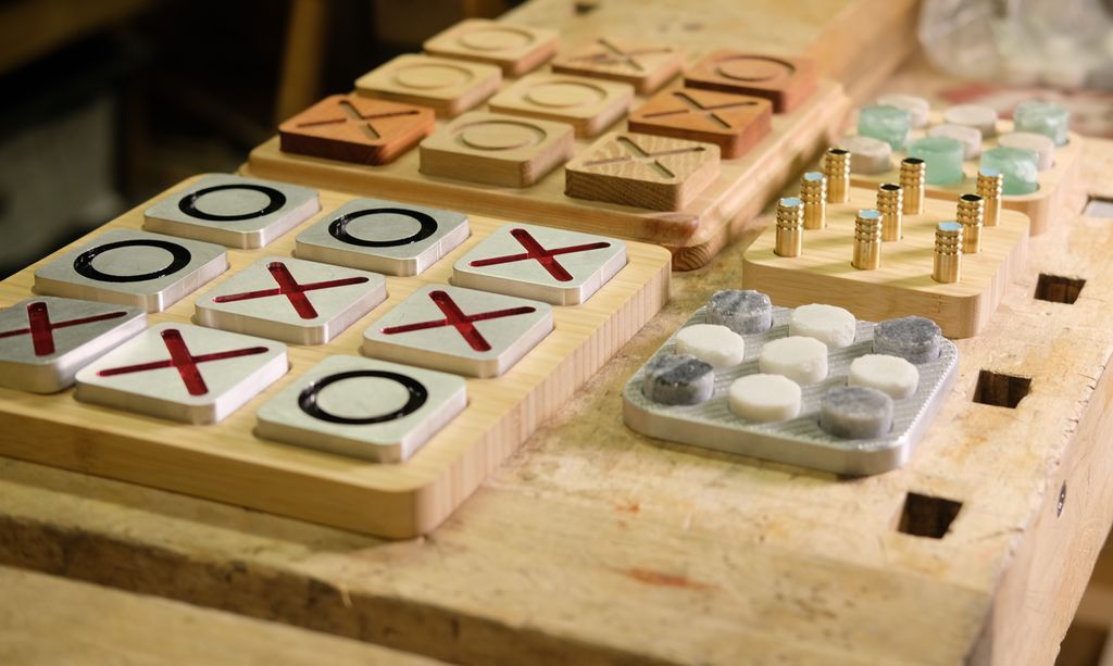 Ei samling av tre-på-rad-spill. Flere ulike design med ulike materialvalg for brett og brikker, for eksempel tre, aluminium, stein og messing. Foto.