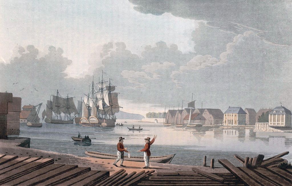 Christiania havn i 1800.  Det er både store seilskuter og små båter i havna. Bebyggelse rundt havna med ulike trebygninger. To menn i forkant ser ut til å diskutere. Trykk.