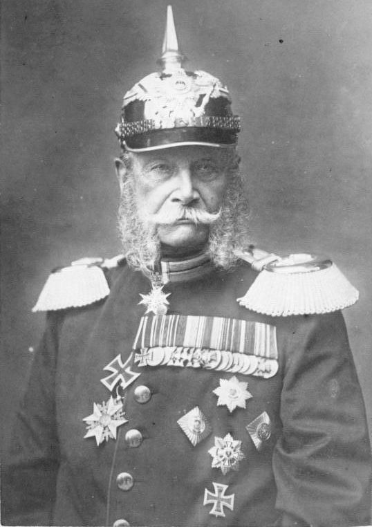 Portrett av den første tyske keiseren, Vilhelm 1. Han har uniform med en mengde medaljer og utmerkelser, prangende epåletter og hjelm med en høy metallpigg på toppen. Foto.