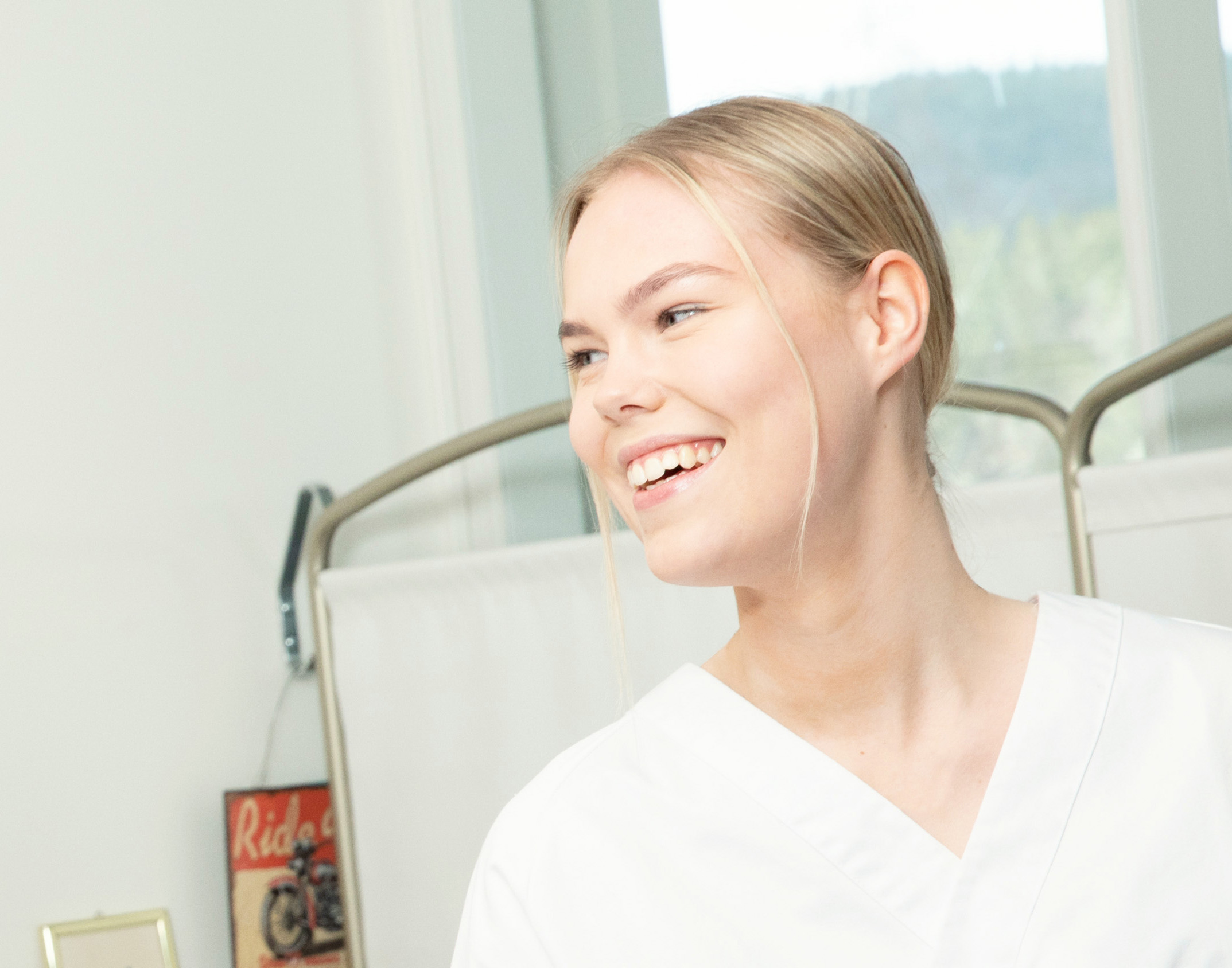 Helsefagarbeider i hvit uniform smiler bredt. Foto.