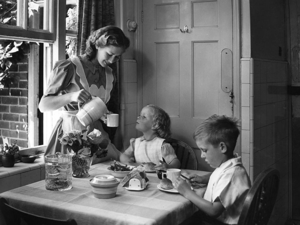 Husmor som serverer frukost til to barn på 1950-talet. Foto.