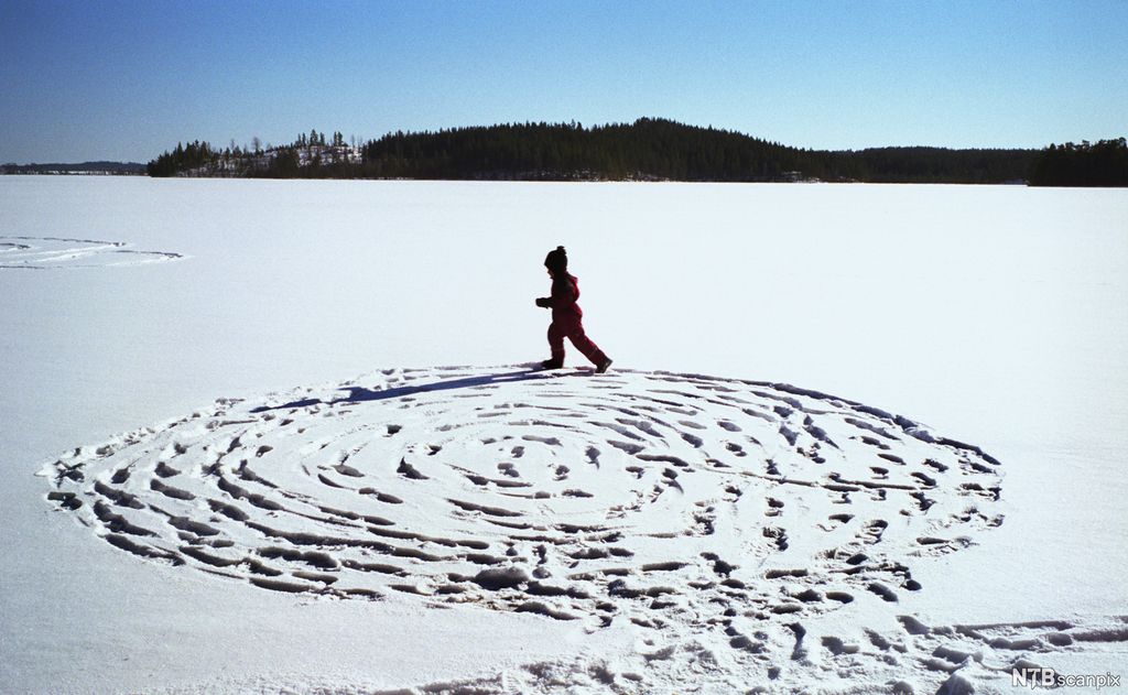 Eit barn lagar snølabyrint på snødekt is. Foto.