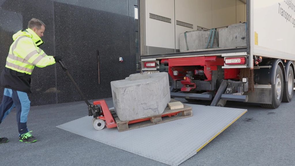 Foto som viser en mann som kjører en jekketralle med last på en bakløfter. 