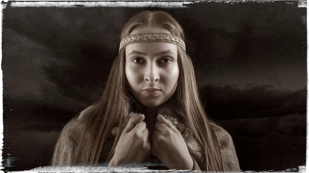 Ung kvinne med langt hår og et dekorert bånd rundt hodet. Hun har på ei kappe som hun holder fast rundt halsen. Mørke skyer i bakgrunnen. Manipulert foto.