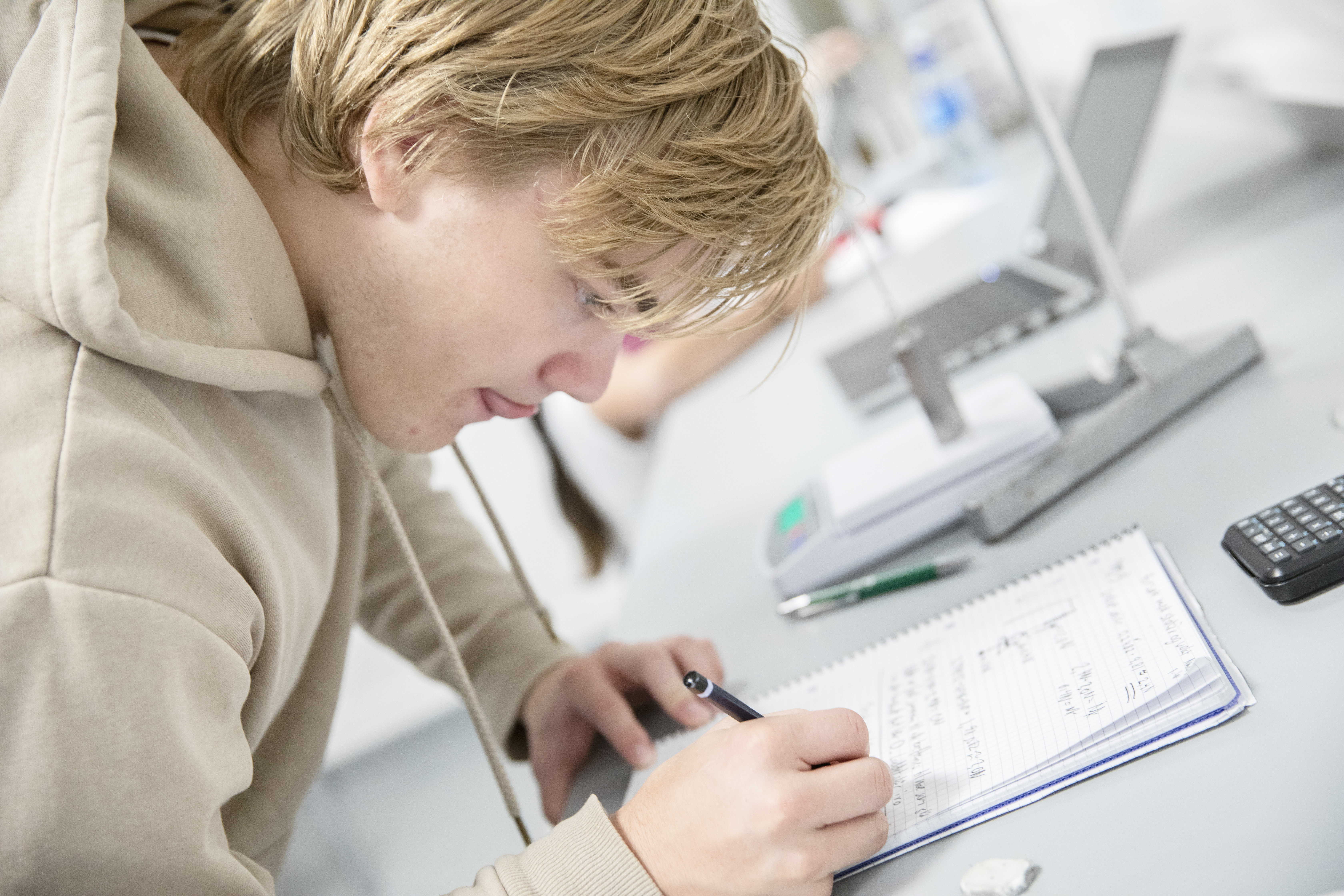 Mannlig elev noterer i notatblokken sin under naturfagsforsøk. Foto.