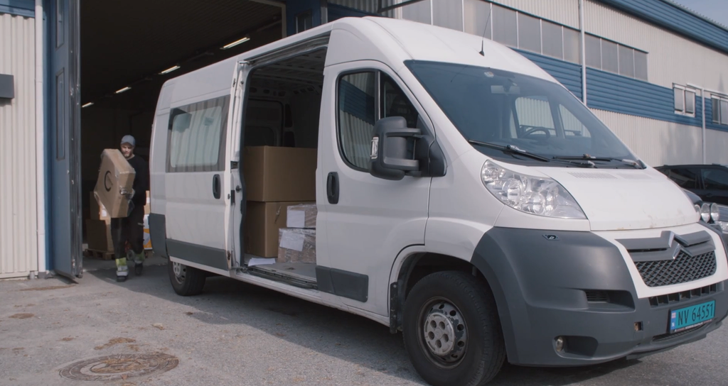 En mann bærer en pappeske ut til en hvit varebil. Skjermdump.