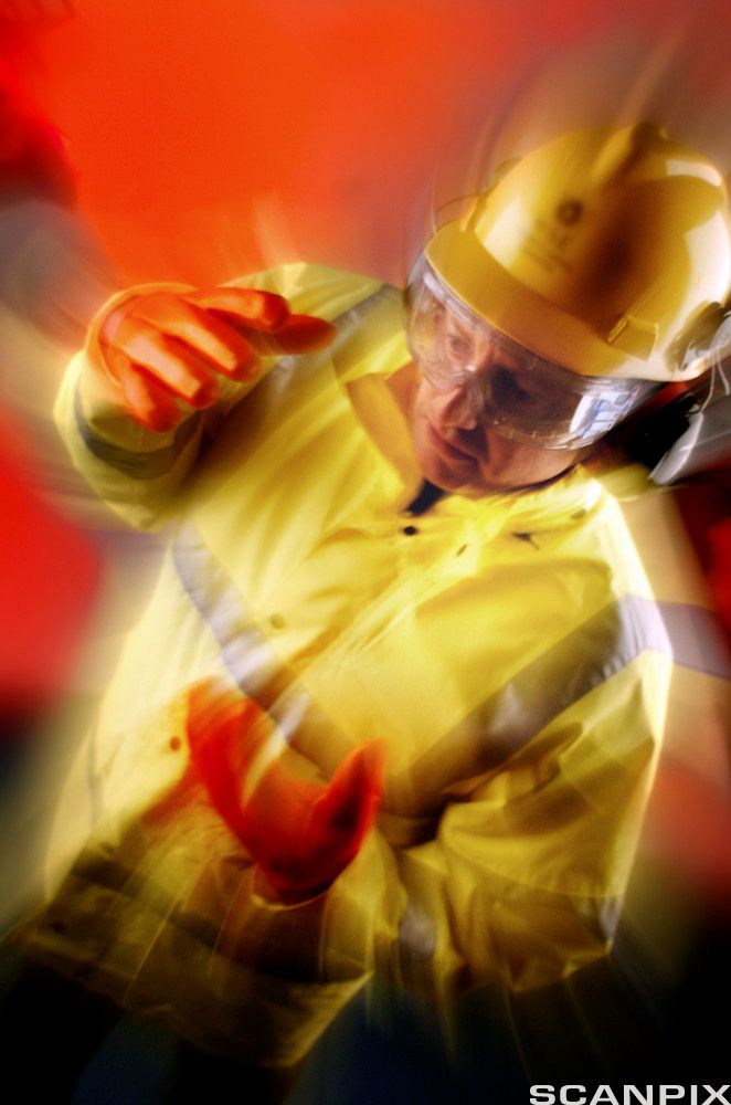 Person med beskyttende arbeidsantrekk. Gul, reflekterende jakke, røde gummihansker, hørselsvern, hjelm og vernebriller.