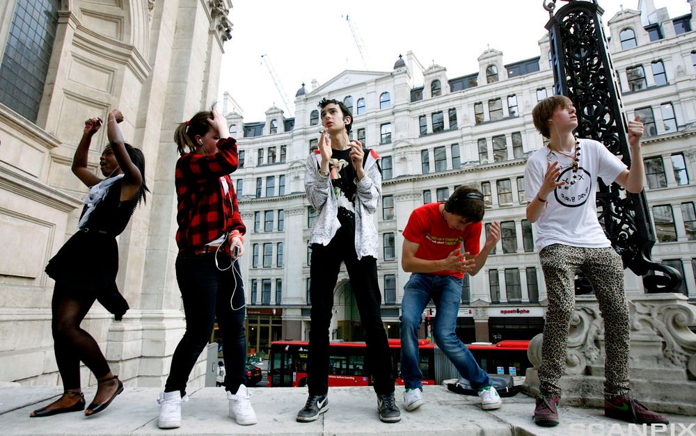 Fem unge mennesker danser utenfor et offentlig bygg.