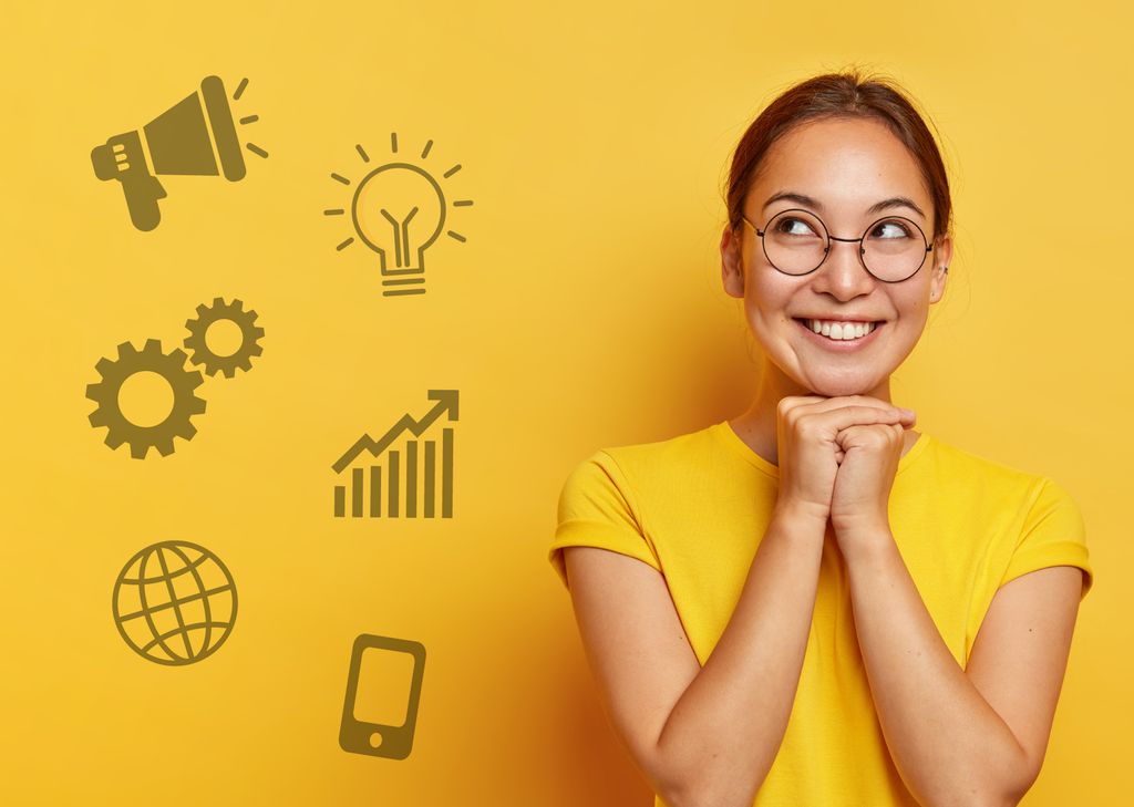 Halvnært utsnitt av ung kvinne i gul t-skjorte som smiler og ser oppover. Bakgrunnen er gul. Foto.