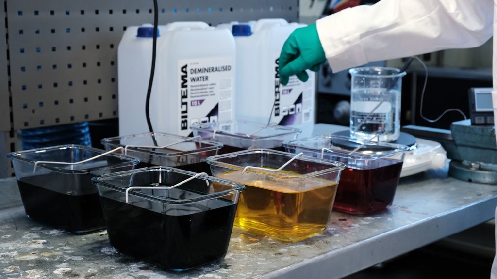 Glassbeholdere med væske av ulik farge som står på en arbeidsbenk. Foto.