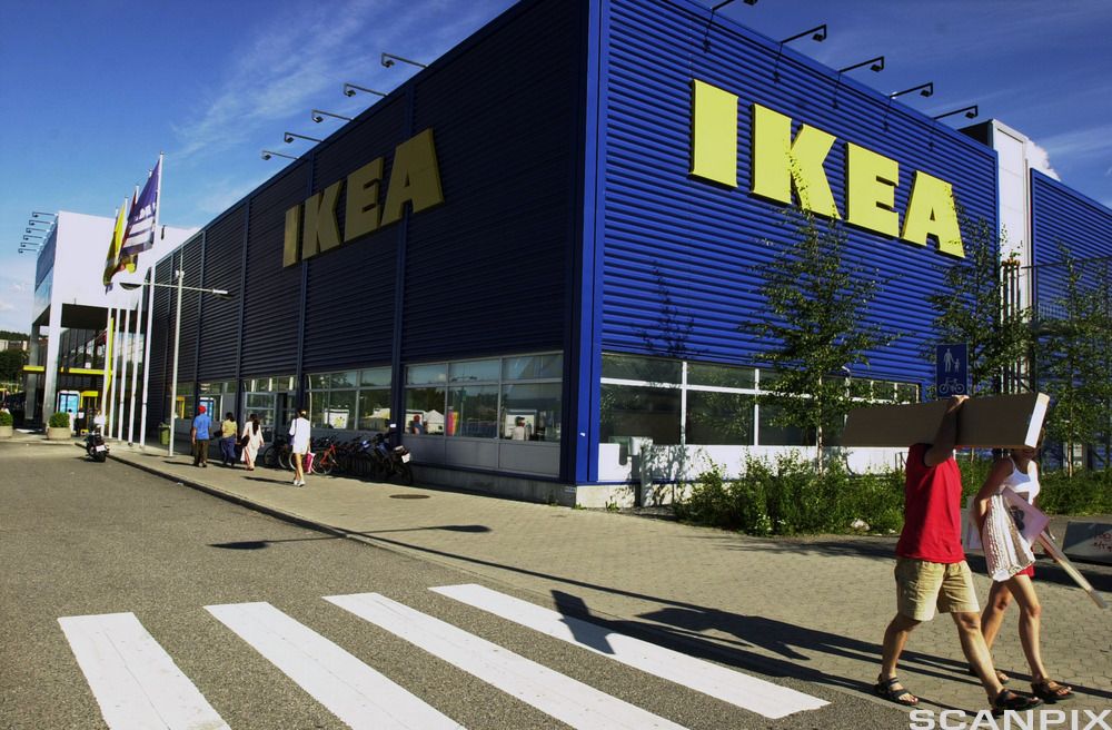 Flere personer passerer utenfor en stor, blå bygning. Det står IKEA med store, gule bokstaver på bygget. Foto.