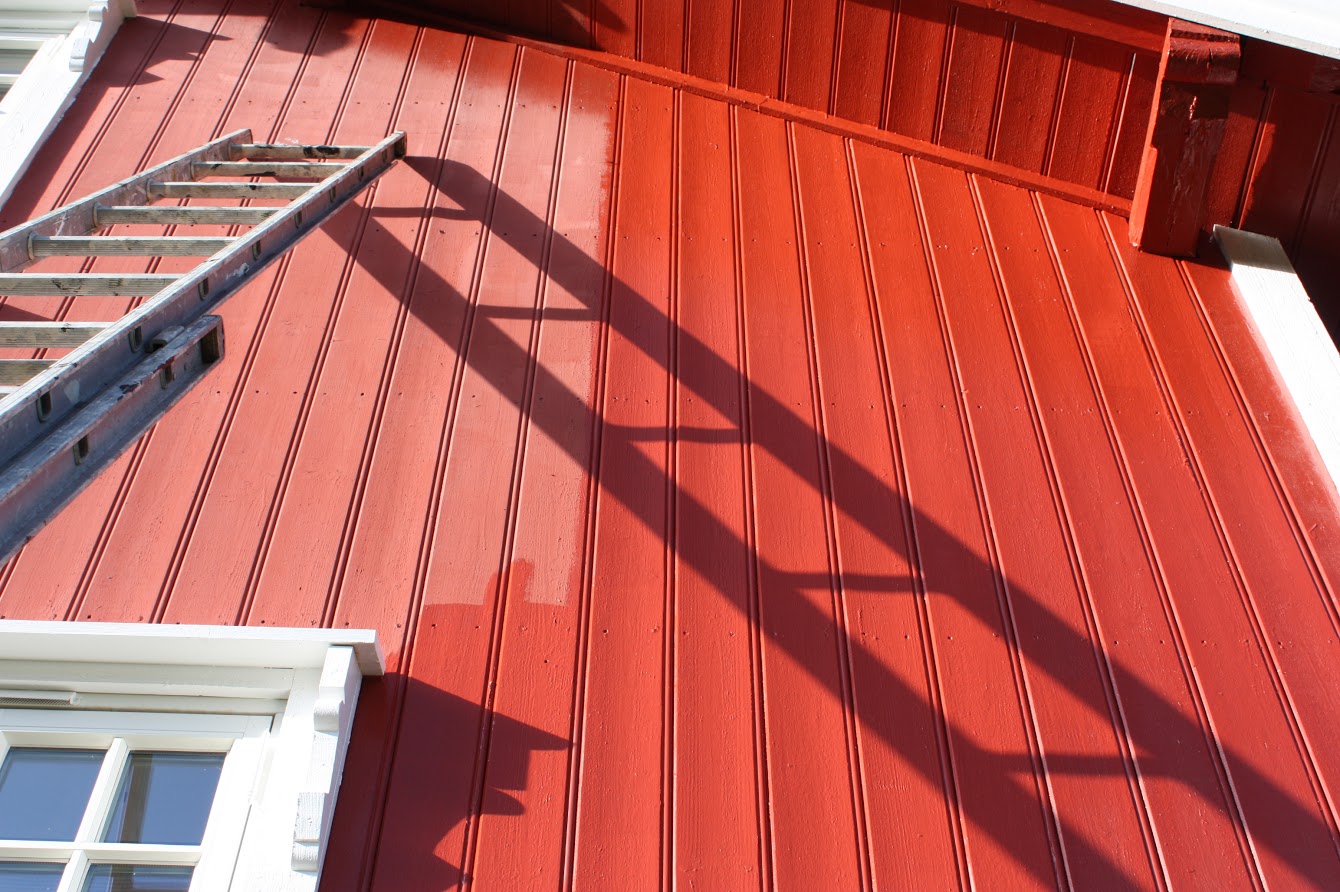 En stige står lent mot en rød vegg som er halvveis malt på nytt. Foto. 