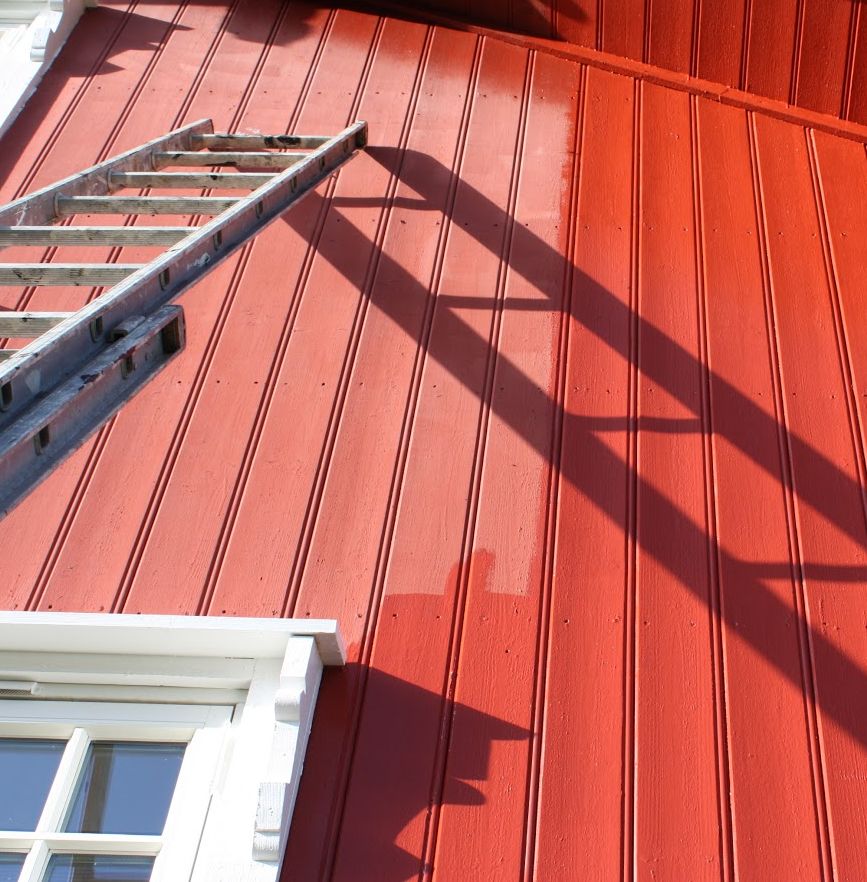 En stige står lent mot en rød vegg som er halvveis malt på nytt. Foto.