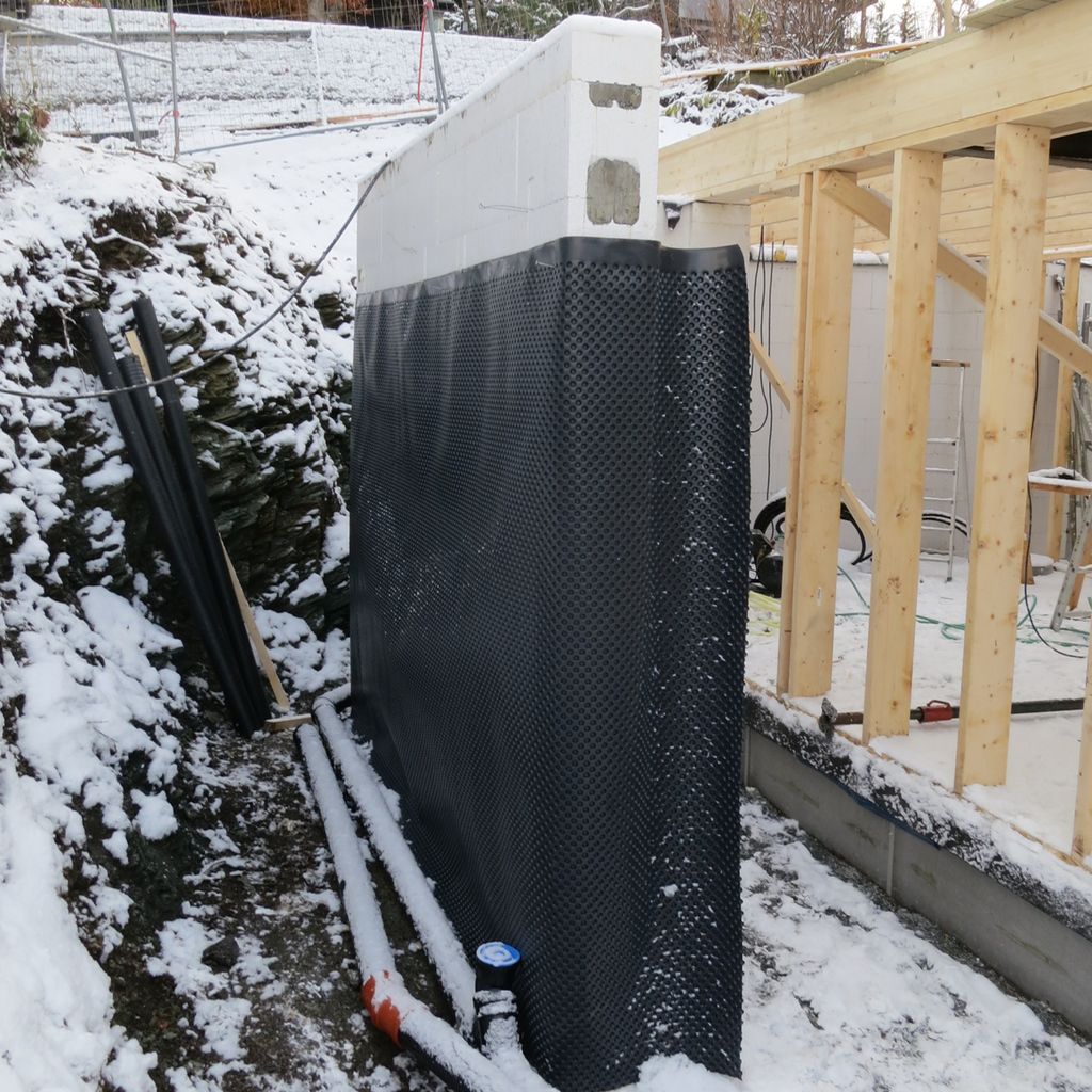 Drensplate på ein grunnmur i ei bygggegrop med snø. Foto.