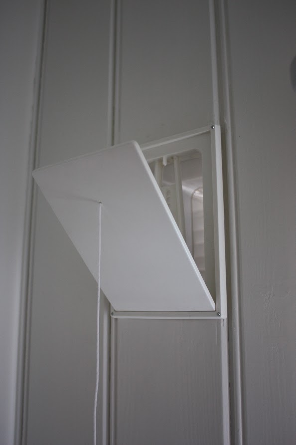 Åpen ventil i en hvit panelvegg innendørs. Foto. 