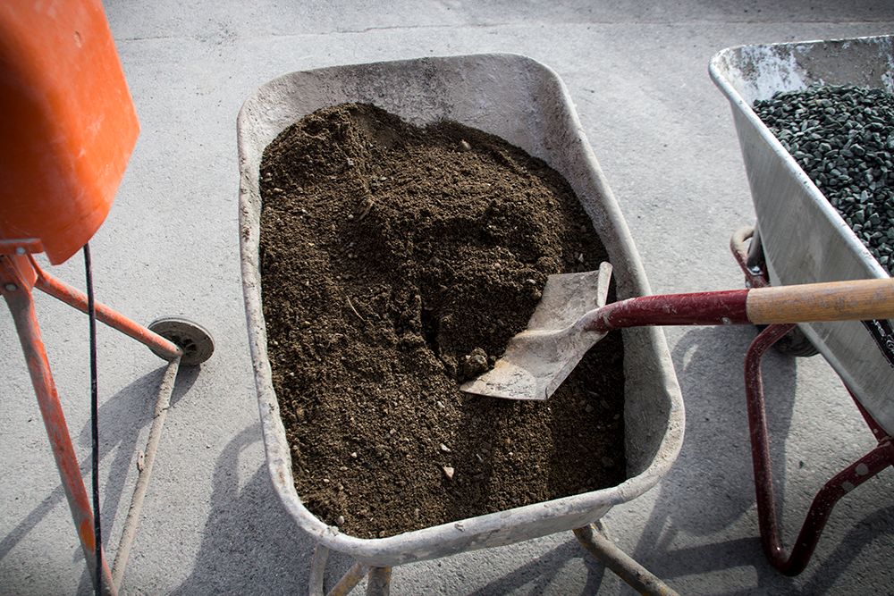 En spade er stukket i sanden i en trillebår. Foto.