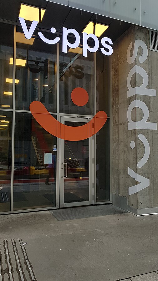 Nærbilde av en kontorbygning. Hvite bokstaver som danner ordet Vipps er montert og lett synlig i front. I-en er formet som et slags smilefjes. Foto.