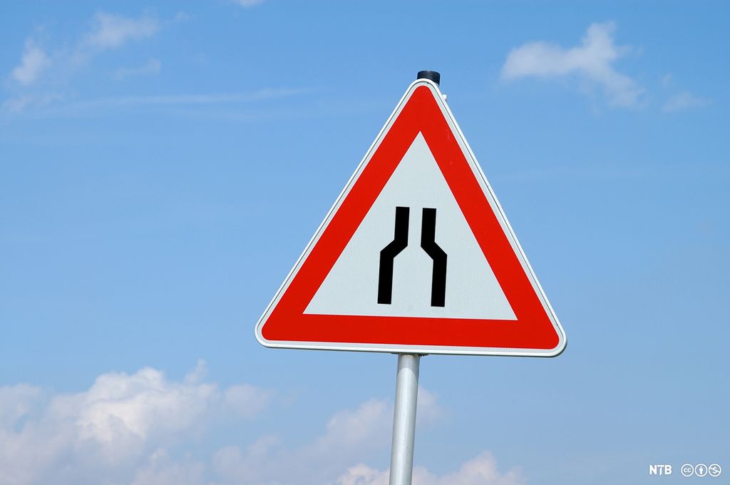 Trekanta skilt med raud kant rundt. To parallelle linjer i midten av skiltet viser at ein veg blir smalare. Foto.