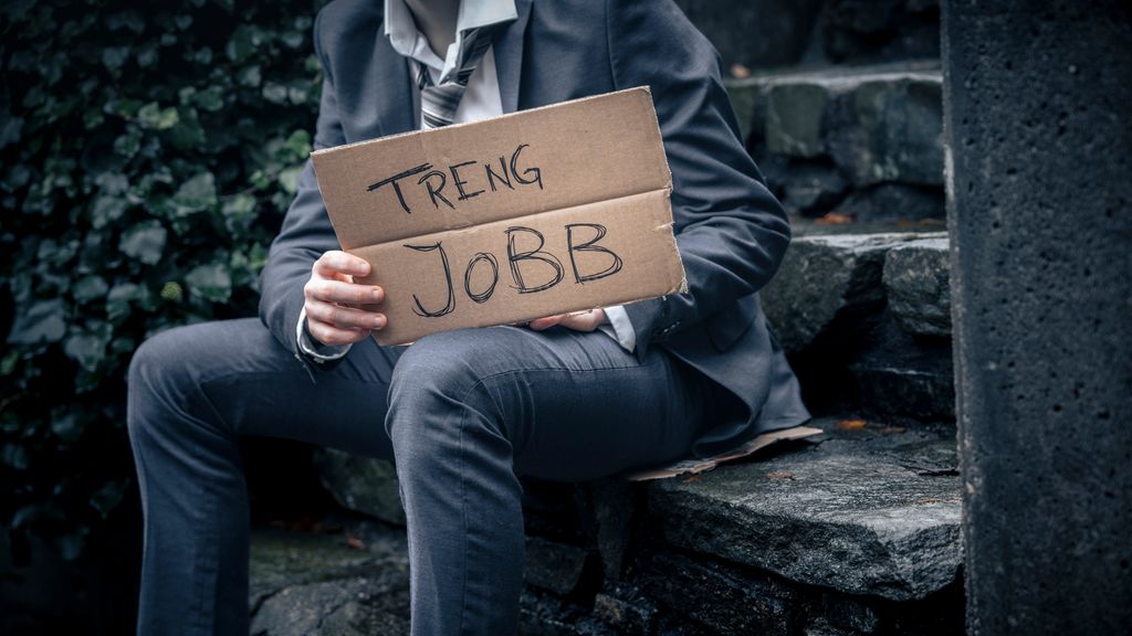 Mann i dress sit på ei trapp og held eit pappskilt der det står “treng jobb”. Foto.