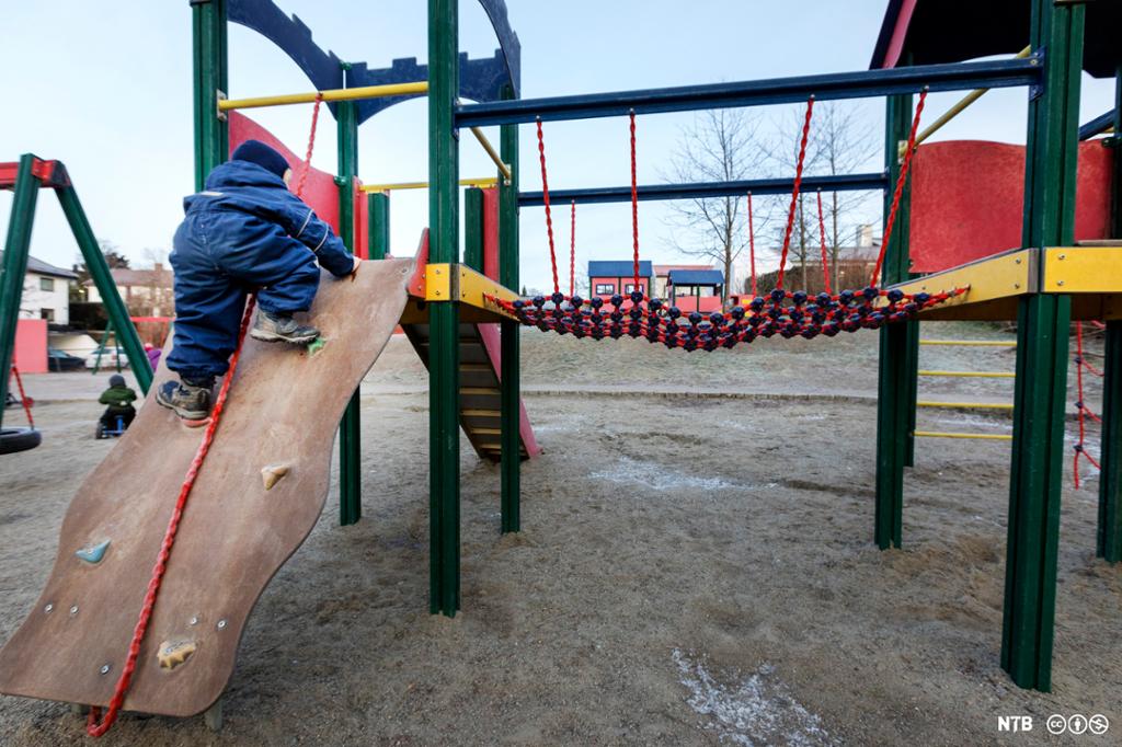 Ein liten gut i parkdress klatrar på eit leikstativ. Foto. 