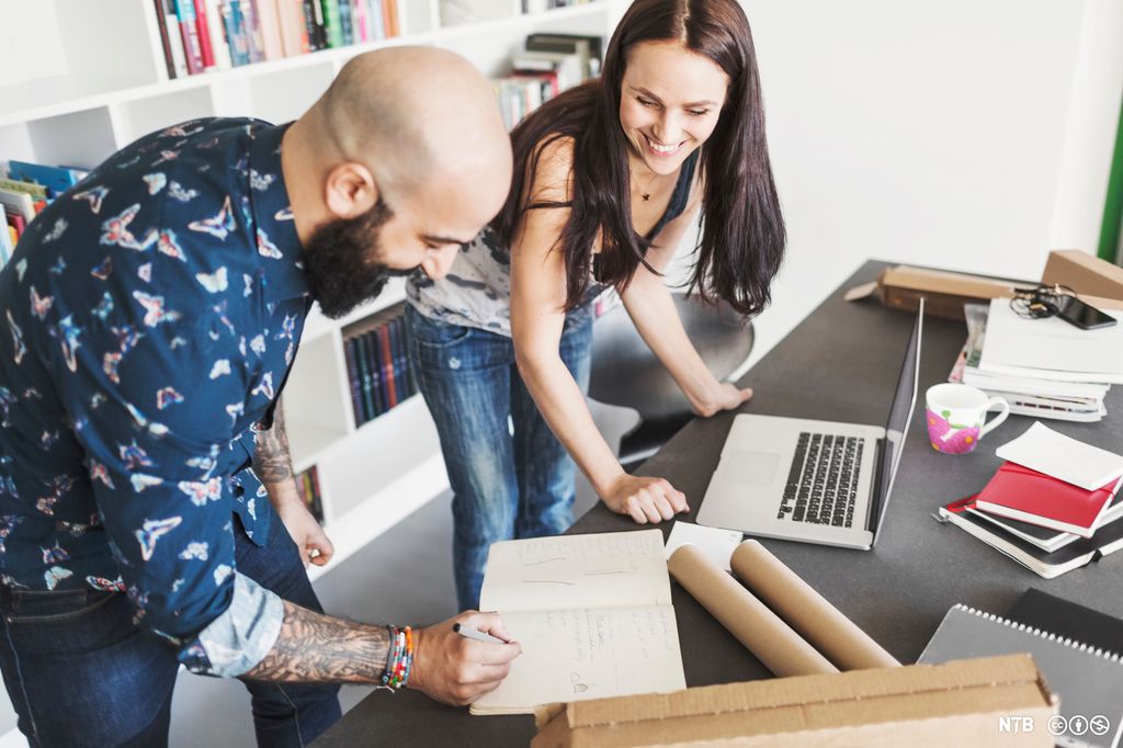 En mann og en kvinne står ved en pult og arbeider. Foto.