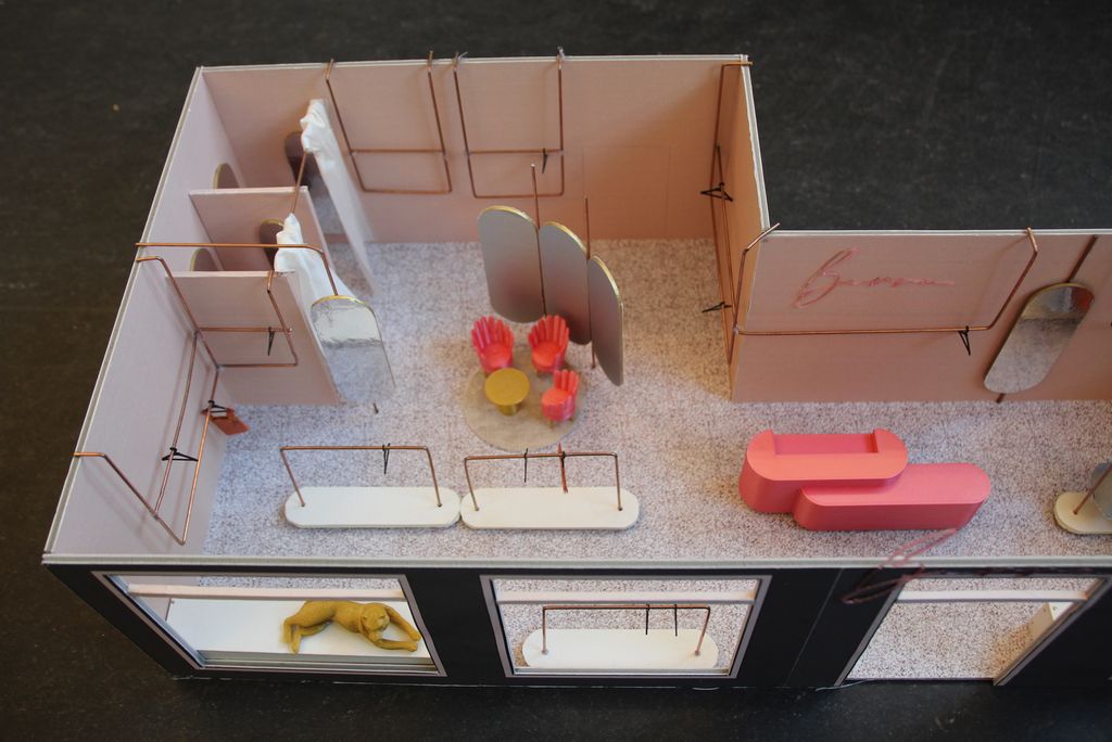 Miniatyrmodell av interiøret i en klesbutikk. Veggene er tynne. Ståltråder er bøyd til som klesstativer. Små stoler og bord av plast er plassert rundt i modellen. Foto.