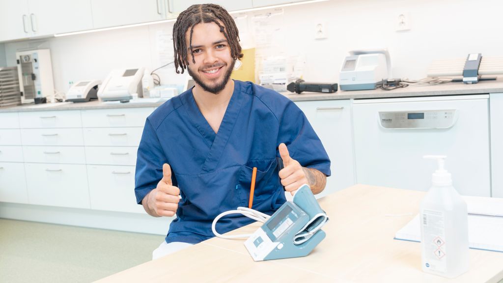 Mann i uniform for helsepersonell med blodtrykksapparat viser tommel opp. Foto.