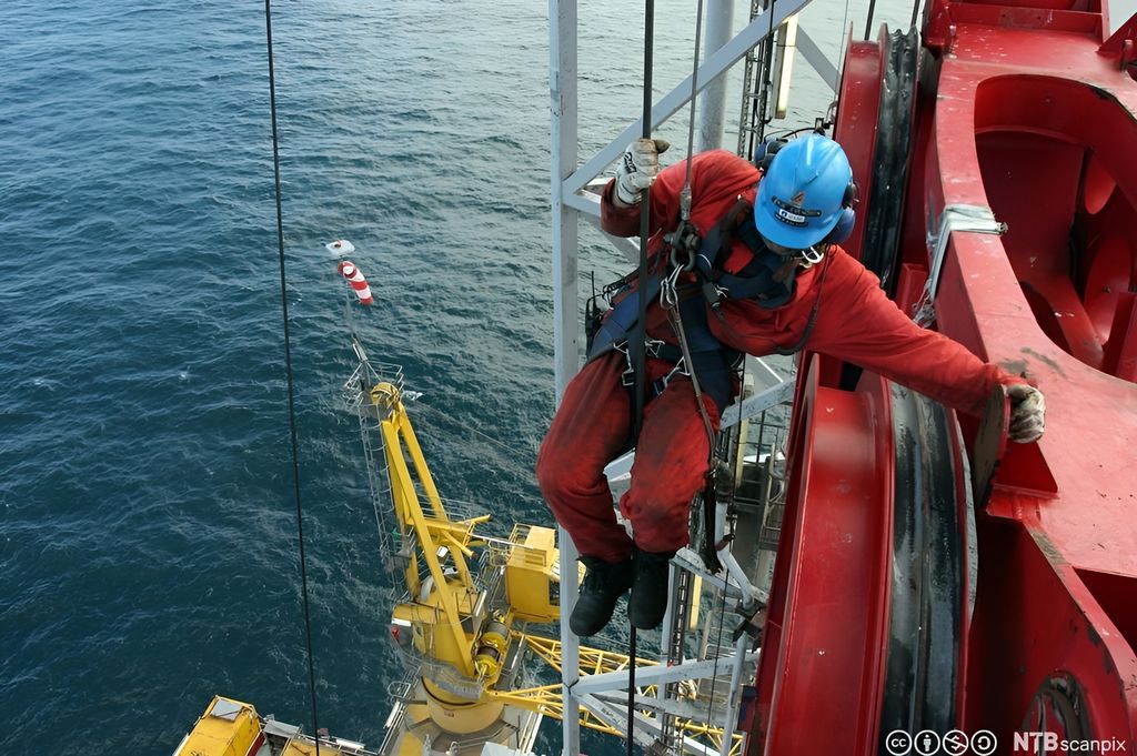 En boredekksarbeider jobber i toppen av ramriggen, boretårnet. Han bruker ridebelte til å sikre seg med. Foto.