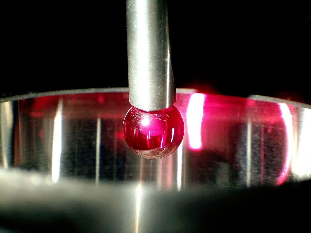 Rød kule på ei sølvfarga stang inne i en sylinder. Foto.