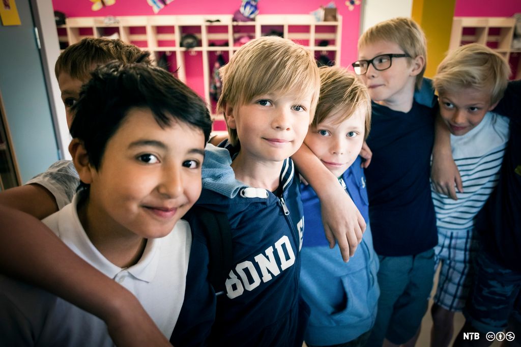 Seks gutter står tett ved siden av hverandre. De holder rundt hverandres skuldre og smiler. Foto.