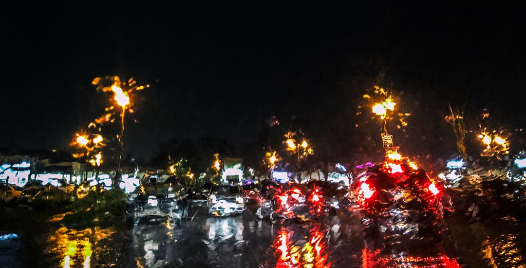 View from a window covered in rain, lights from cars, street lights, and buildings. Photo.