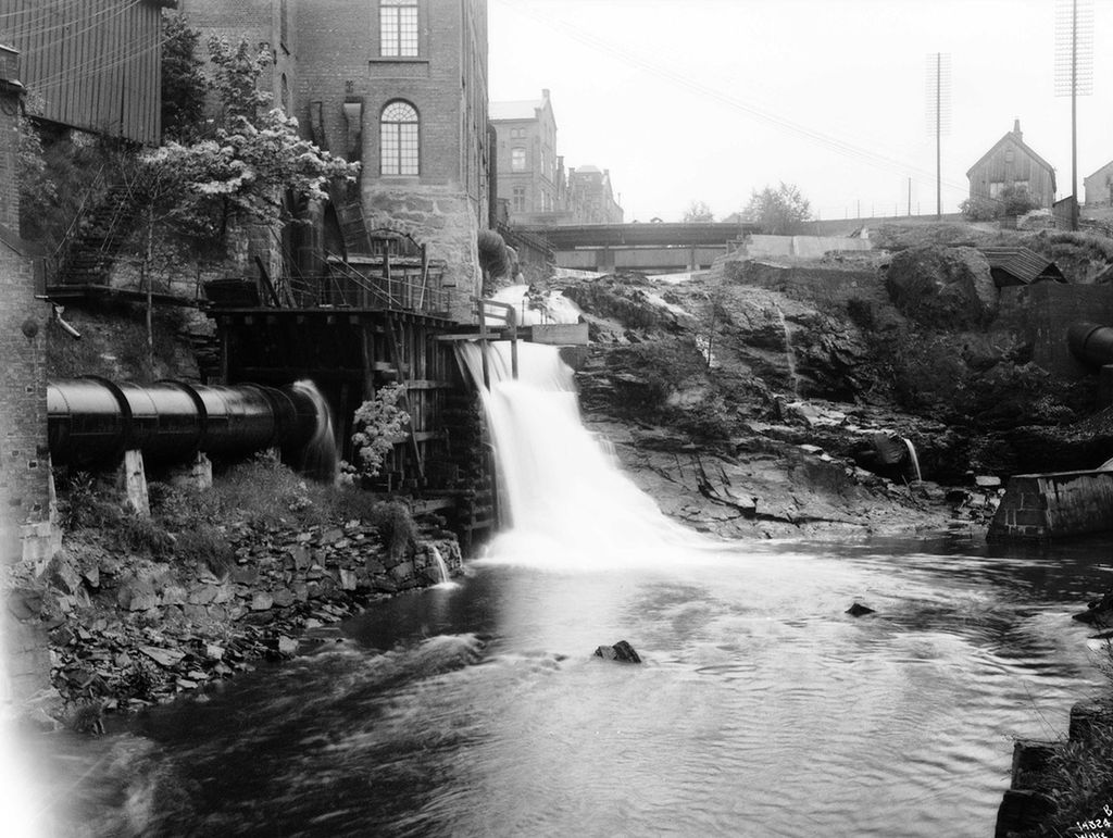 Industribygninger ved fossefall i Akerselva. En bro krysser elva lenger opp. Foto.