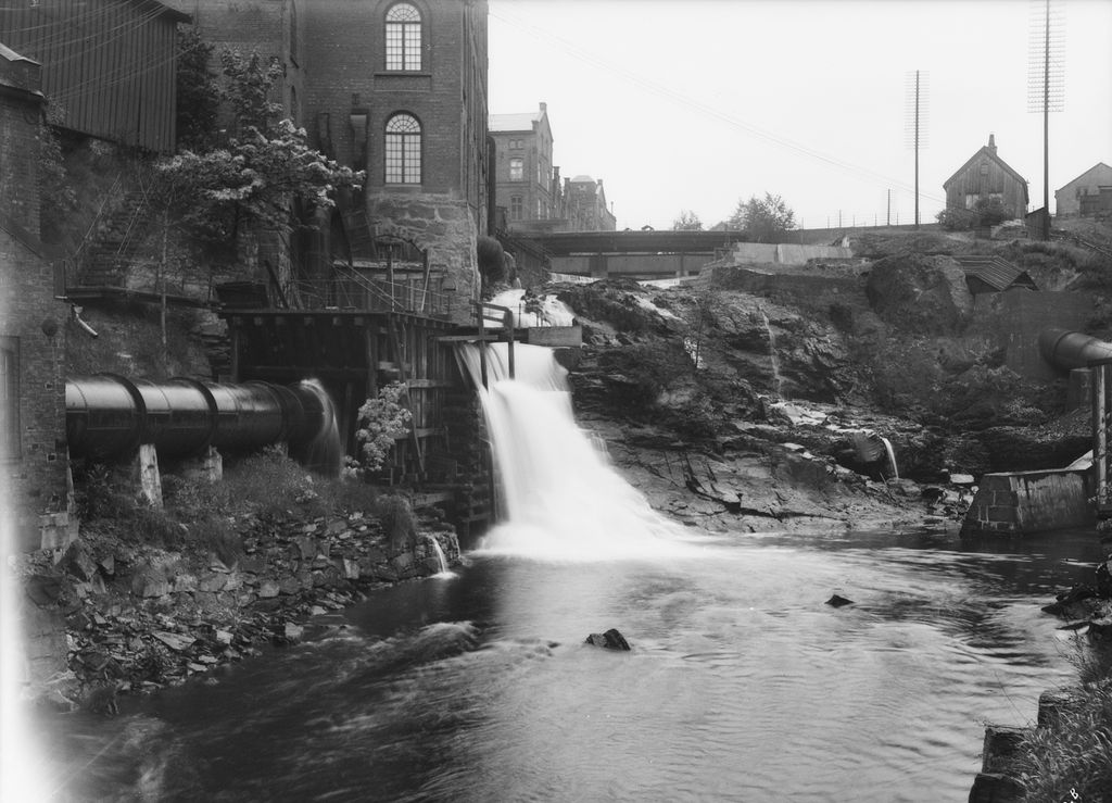 Industribygninger ved fossefall i Akerselva. En bro krysser elva lenger opp. Foto.