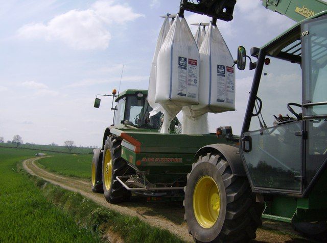 Traktor fyller kunstgjødsel fra storsekker ned i gjødselsprederen på en annen traktor. Foto.