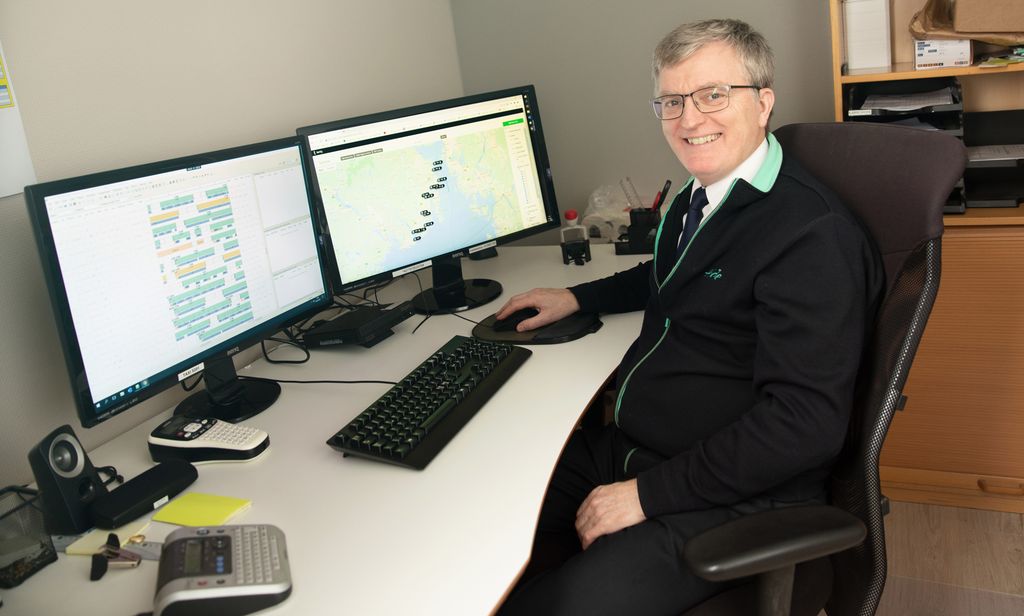 Bildet viser en mann som arbeider med ruteplanlegging for bussruter ved kontorpulten sin.