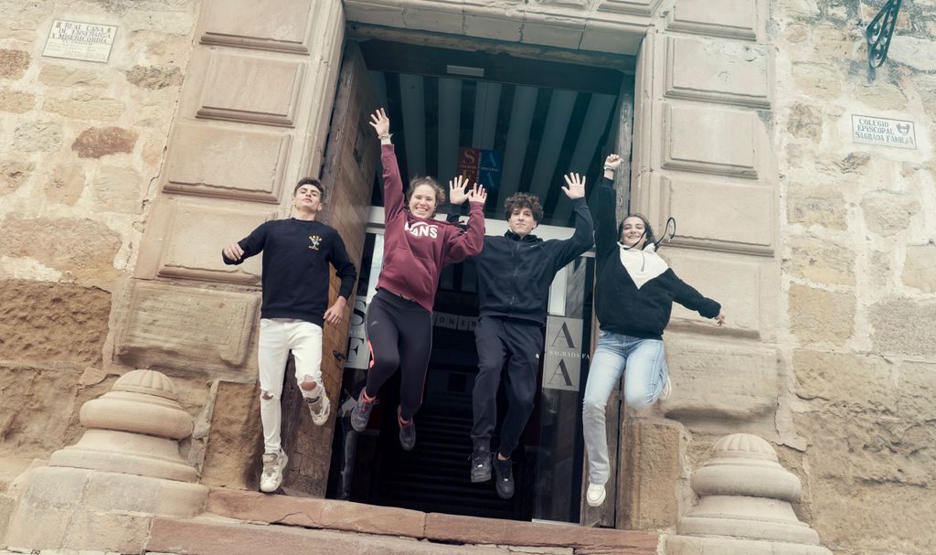 Fire ungdommer hopper ut av ei stor inngangsdør. Foto.