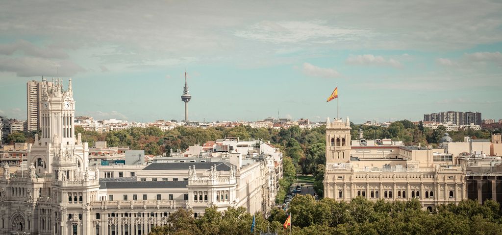 Oversiktsbilde av monumentale bygninger, trær og et tv-tårn i det fjerne i en storby. Det spanske flagget vaier over en av bygningene. Foto.