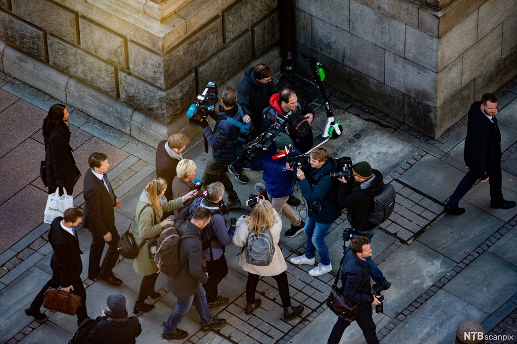 Kvinne omringet av journalister med mikrofoner og kameraer på et gatehjørne. Foto.