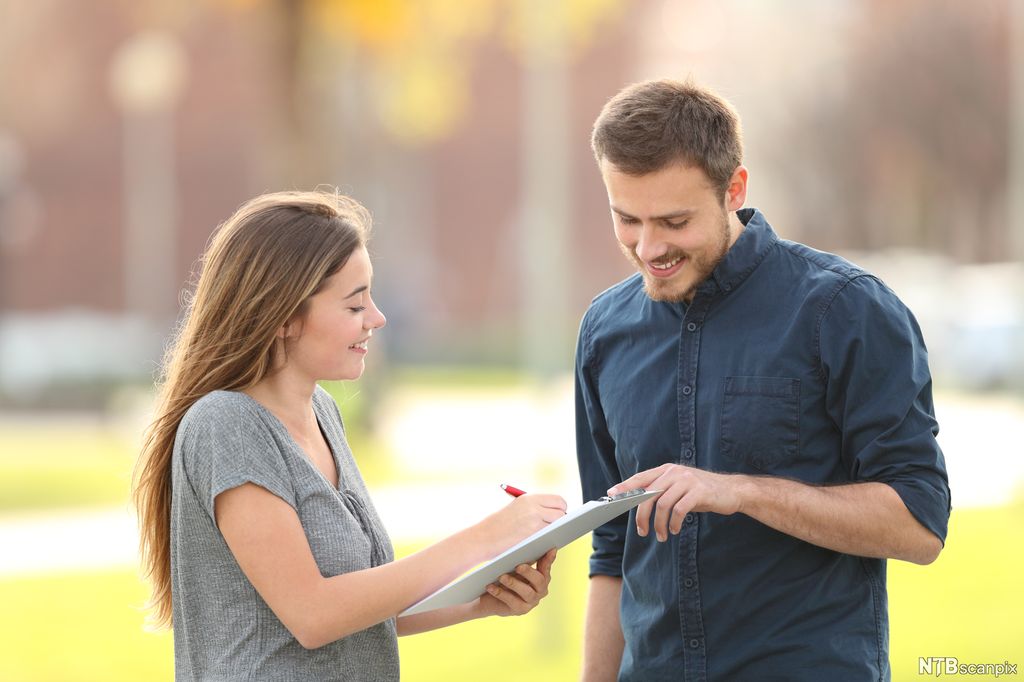 Jente med skjema henvender seg til en mann. Foto.