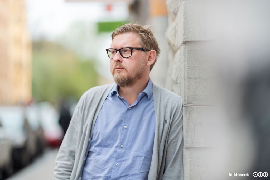 Stående mann med briller ser ettertenksomt mot venstre. Foto.