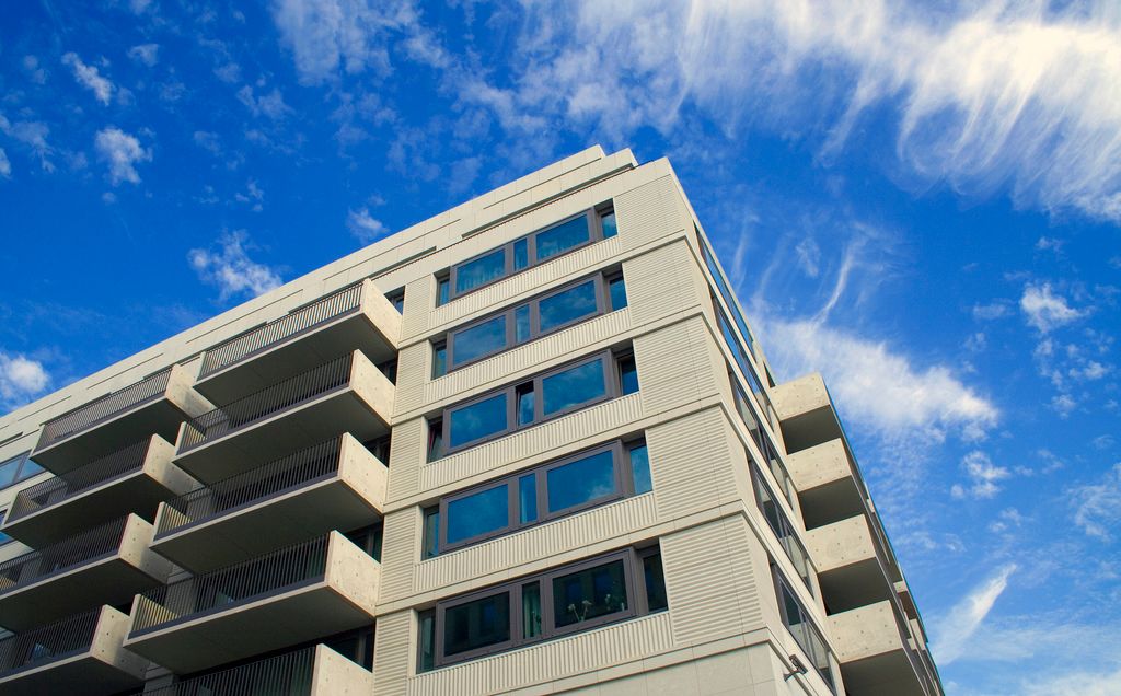 Boligblokk med betong og glassfasade sett fra froskeperspektiv med blå himmel over. Foto.