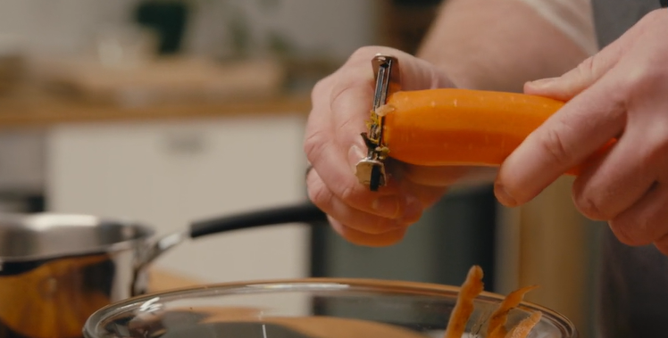 En gulrot skrelles i enden med en gulrotskreller. Foto.