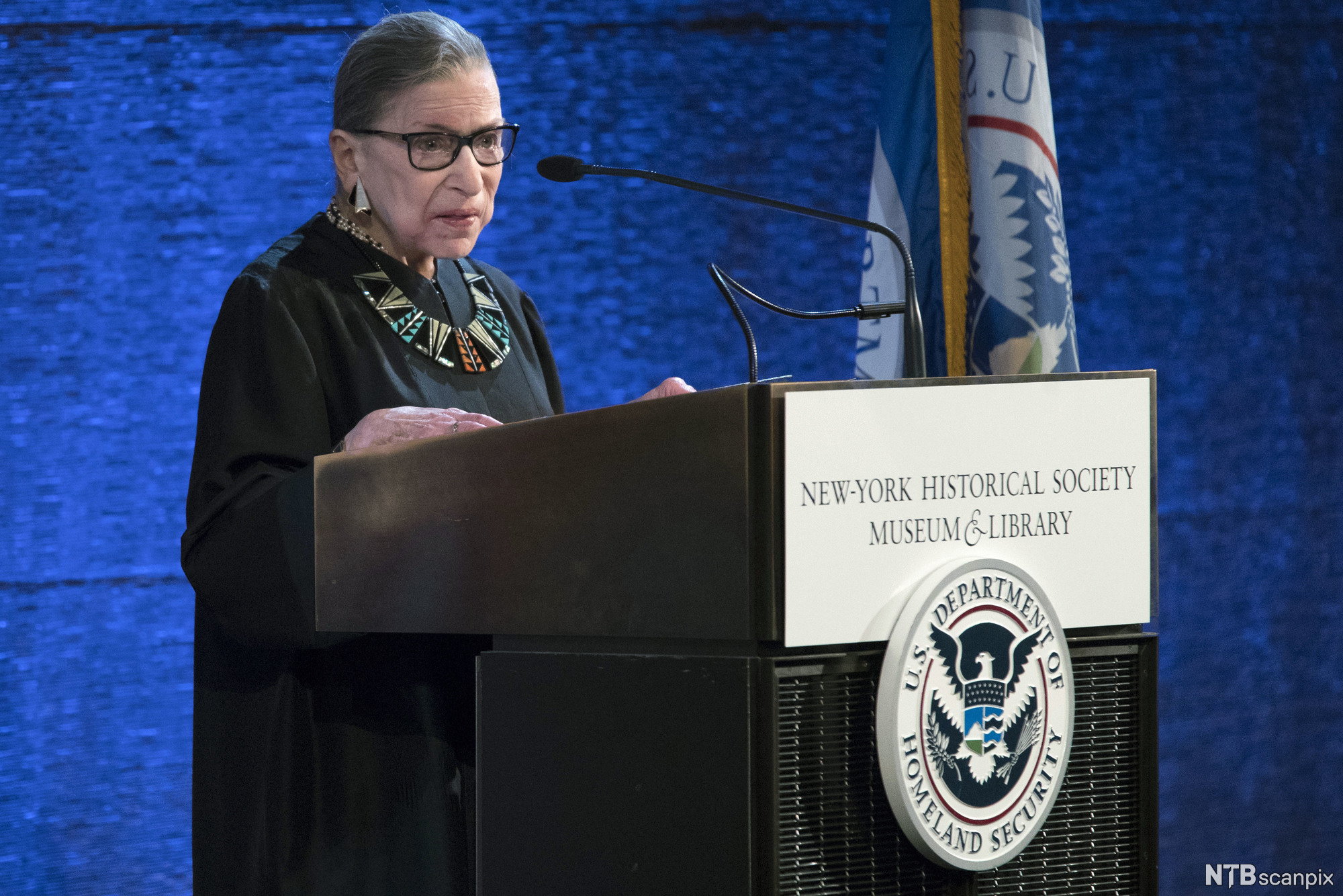 Ruth Bader Ginsburg standing behind a microphone. Photo.