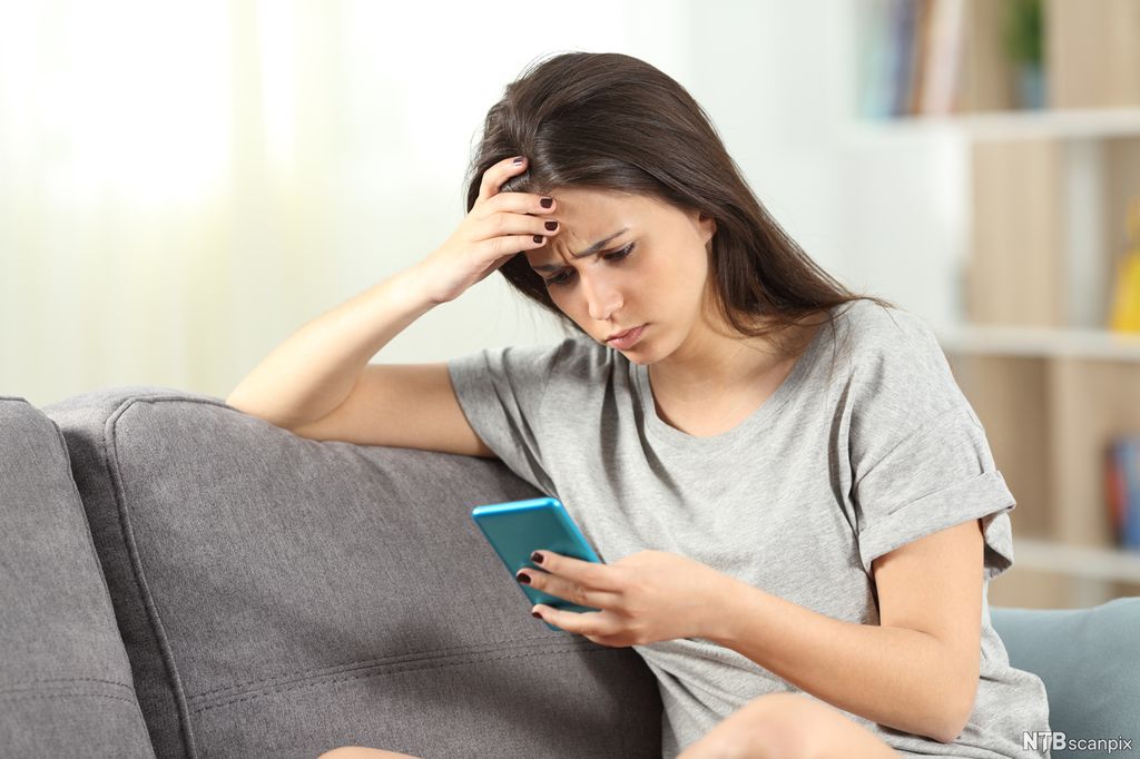 En ung kvinne ser fortvilet på mobiltelefonen. Foto.