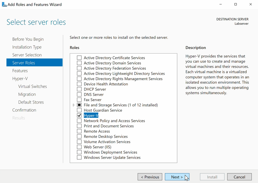 Skjermvindu med tittelen "Select server roles" med ei lang liste med tjenester (roller) som kan installeres. Ved hver tjeneste i lista er det en avkrysningsboks. Ved tjenesten Hyper-V er det satt en hake. Musepekeren er over knappen "Next" nederst på siden. Skjermbilde.
