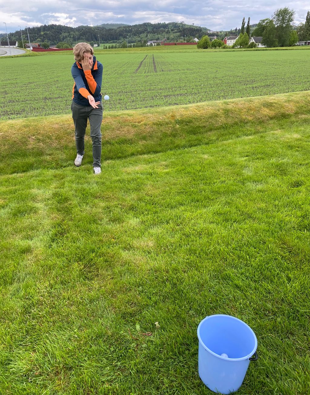 Ungdom holder seg for det ene øyet og kaster samtidig ball mot ei bøtte. Foto.