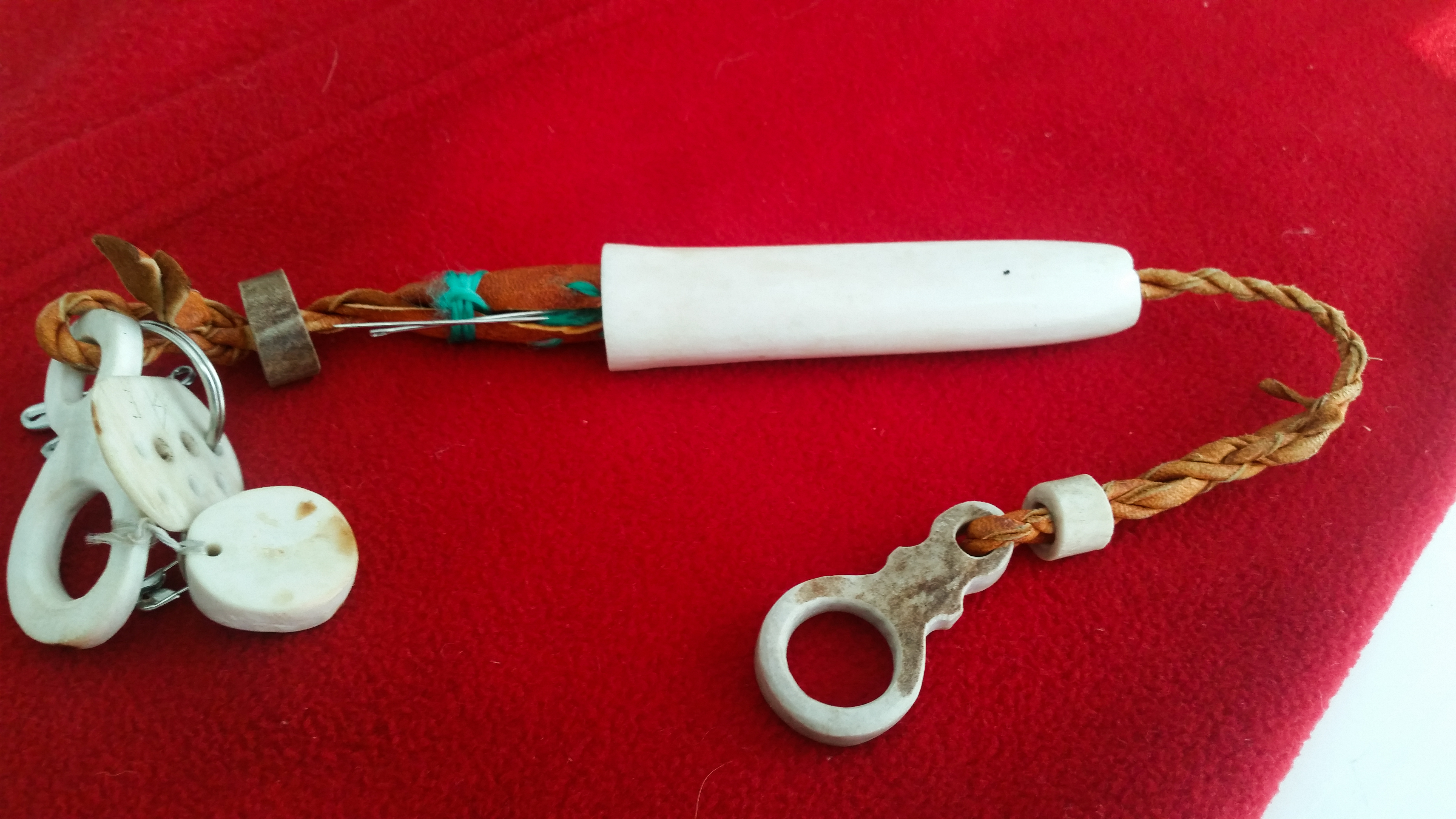 Et uthulet stykke bein. Gjennom beinet er det trædd ei skinnreim som en kan feste synåler i. 