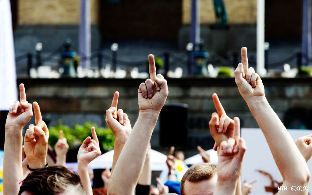 Mange hender i luften viser langfingeren under en demonstrasjon. Foto.